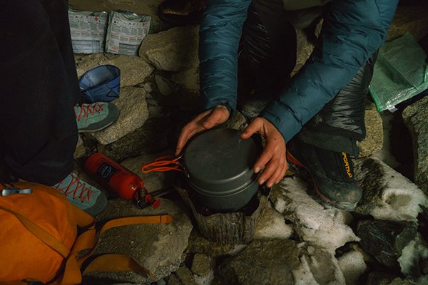 Mayan Smith-Gobat warms her hands while brewing up some hot tea in the cold bivy cave at the base of Torre Central in Patagonia
