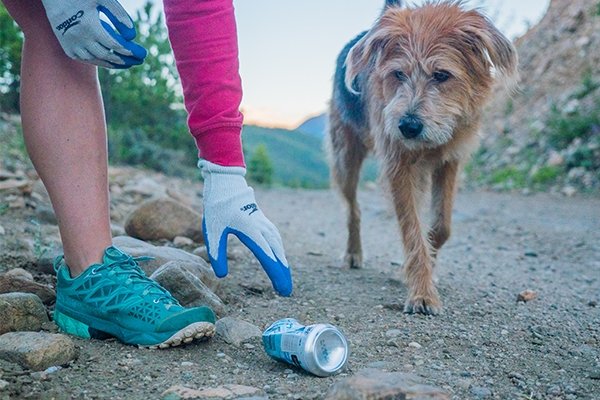 Volunteer with dog cleaning up aluminum can off trail